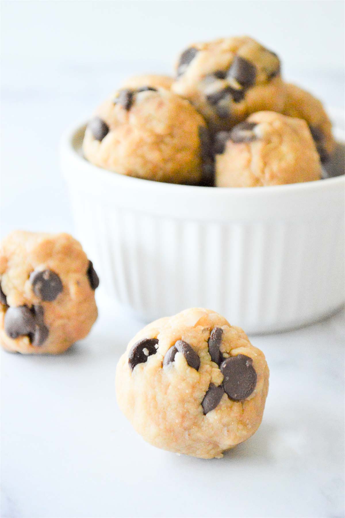 Two tahini chocolate chip energy balls set on countertop in front of bowl of energy balls