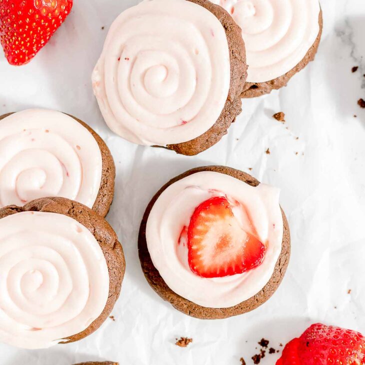 Overhead view of frosted strawberry cheesecake cookies with fresh strawberries